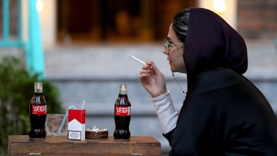 An Iranian smokes a Marlboro cigarette while two Coca-Cola stand on her table at a cafe in downtown Tehran, Wednesday, July 10, 2019.