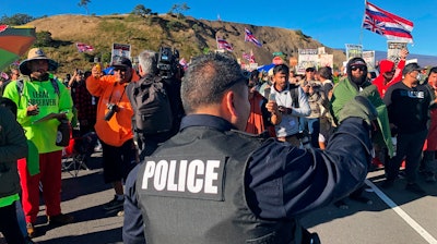 A police officer gestures at demonstrators blocking a road at the base of Hawaii's tallest mountain, Monday, July 15, 2019, in Mauna Kea, Hawaii.