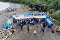 In this Tuesday, July 16, 2019, drone photo released by the University of Alaska Fairbanks and Alaska Center for Energy and Power, Gov. Mike Dunleavy, center rear, poses for photos in front of a Riv-Gen Power System turbine on the bank of the Kvichak River in Igiugig, Alaska. A tiny Alaska Native village is adopting an emerging technology to transform the power of a local river into a renewable energy source.