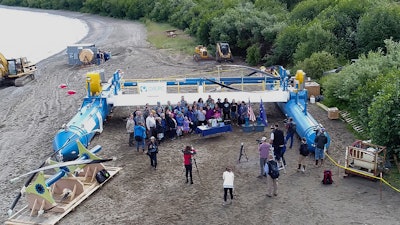 In this Tuesday, July 16, 2019, drone photo released by the University of Alaska Fairbanks and Alaska Center for Energy and Power, Gov. Mike Dunleavy, center rear, poses for photos in front of a Riv-Gen Power System turbine on the bank of the Kvichak River in Igiugig, Alaska. A tiny Alaska Native village is adopting an emerging technology to transform the power of a local river into a renewable energy source.