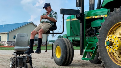 In this July 10, 2019, photo, farmer Mark Hosier, 58, uses a lift to get into a tractor on his farm in Alexandria, Ind.