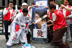 A protester uses scissors to cut an image of Japanese Prime Minister Shinzo Abe during a rally in Seoul, Tuesday, July 23, 2019.