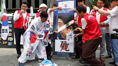 A protester uses scissors to cut an image of Japanese Prime Minister Shinzo Abe during a rally in Seoul, Tuesday, July 23, 2019.
