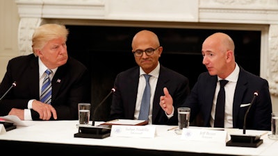In this June 19, 2017, file photo President Donald Trump, left, and Satya Nadella, Chief Executive Officer of Microsoft, center, listen as Jeff Bezos, Chief Executive Officer of Amazon, speaks during an American Technology Council roundtable in the State Dinning Room of the White House in Washington. Amazon and Microsoft are battling for a $10 billion opportunity to build the U.S. military its first “war cloud.”