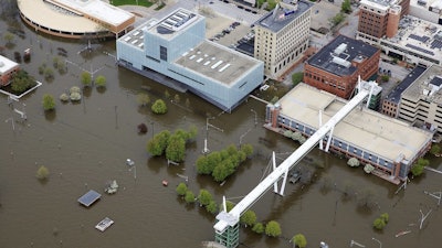 In this Friday, May 3, 2019 aerial file photo of Davenport, Iowa, the Figge Art Museum and the SkyBridge are surrounded by Mississippi River flood waters. Officials in the eastern Iowa city say the city is building a bigger flood barrier in the wake of an April breach that sent floodwaters rushing into downtown streets. Davenport City Administrator Corri Spiegel tells the Quad-City Times that the city will build larger flood walls when there is a high probability the river cresting above 21 feet. Days after the last temporary barrier broke on April 30, the river hit a historic crest of 22.7 feet.