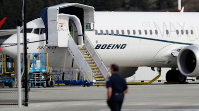 In this March 14, 2019, file photo, a worker walks next to a Boeing 737 MAX 8 airplane parked at Boeing Field in Seattle. Boeing said Thursday, July 18, it will take a $4.9 billion charge to cover possible compensation to airlines whose Max jets remain grounded after two deadly accidents.