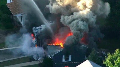 In this Sept. 13, 2018 file image from video provided by WCVB in Boston, flames consume the roof of a home following an explosion in Lawrence, Mass. Columbia Gas of Massachusetts and its parent, NiSource Inc., announced Monday, July 29, 2019, a settlement had been reached in class action lawsuits resulting from the disaster across several towns north of Boston.