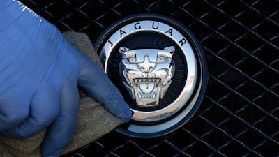 In this file photo dated Wednesday, Sept. 28, 2016, a worker polishes a Jaguar logo on a car at a Jaguar dealer outlet in London. Jaguar Land Rover has announced Friday July 5, 2019, it will retool with new equipment at Castle Bromwich, in central England, to manufacture an all-electric version of the Jaguar XJ sedan car in the U.K.