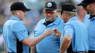 Home plate umpire Brian deBrauwere, left, huddles with officials while wearing an earpiece connected to a ball and strikes calling system prior to the start of the Atlantic League All-Star minor league baseball game, Wednesday, July 10, 2019, in York, Pa. deBrauwere wore the earpiece connected to an iPhone in his ball bag which relayed ball and strike calls upon receiving it from a TrackMan computer system that uses Doppler radar. The independent Atlantic League became the first American professional baseball league to let the computer call balls and strikes during the all star game.