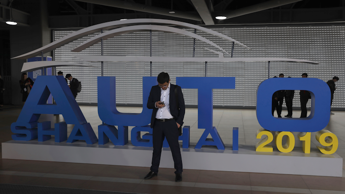 In this April 16, 2019, file photo, a man waits near a sign for the Auto Shanghai 2019 show in Shanghai.