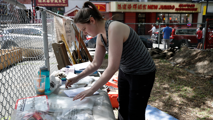 In this July 8, 2019 file photo Sarah Keklak, archaeology lab manager for the city of Boston, sorts samples at the first historical excavation, in Boston's Chinatown. The archaeological dig has been cut short after it turned up a 1980s music cassette, a toy dinosaur and other bric-a-brac. The city's Archaeology Program tweeted Tuesday, July 30, that it was wrapping up its three-week excavation at a vacant lot near the neighborhood's distinctive gateway because researchers have reached the water table, and it is unsafe to dig further.