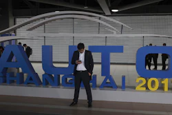 In this April 16, 2019, file photo, a man waits near a sign for the Auto Shanghai 2019 show in Shanghai.