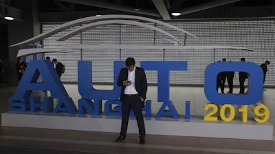 In this April 16, 2019, file photo, a man waits near a sign for the Auto Shanghai 2019 show in Shanghai.