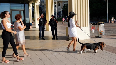 Tourists walk on the beach promenade as police officers stand guard ahead of the upcoming G7 Summit in Biarritz, France, Thursday, Aug. 22, 2019.