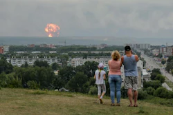 In this photo taken on Monday, Aug. 5, 2019, a family watches explosions at a military ammunition depot near the city of Achinsk, Russia.