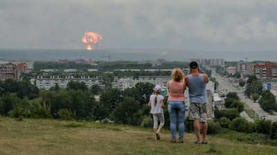 In this photo taken on Monday, Aug. 5, 2019, a family watches explosions at a military ammunition depot near the city of Achinsk, Russia.