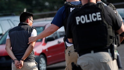 In this Aug. 7, 2019, file photo, a man is taken into custody at a Koch Foods Inc. plant in Morton, Miss. Unauthorized workers are jailed or deported, while the managers and business owners who profit from their labor often aren't. Under President Donald Trump, the numbers of owners and managers facing criminal charges for employing unauthorized workers have stayed almost the same.