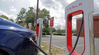 In this July 19, 2019 file photo, a Tesla vehicle charges at a Tesla Supercharger site in Charlotte, N.C. Tesla owners can now buy insurance policies from the electric car company in what may be an essential step toward it selling driverless vehicles. The company says it’s now selling policies in California and will go nationwide at an undisclosed date.