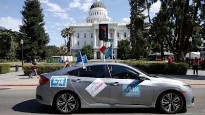 In this photo taken Aug. 28, 2019, a supporter of a measure to limit when companies can label workers as independent contractors drives past the Capitol during a rally in Sacramento.
