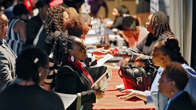 In this Aug. 14, 2019, file photo, representatives from Verizon, Goodwill, Kaiser Permanente and UPS talk with potential applicants during a job fair in Atlanta.