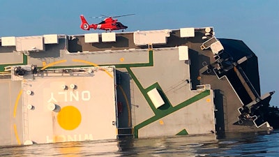 In this image released by the U.S. Coast Guard, a USCG helicopter hovers over an overturned cargo ship in St. Simons Sound, Ga., Monday, Sept. 9, 2019. The U.S. Coast Guard says rescuers have heard noises from inside the ship where multiple crew members are missing after their huge vessel overturned and caught fire off Georgia's coast.