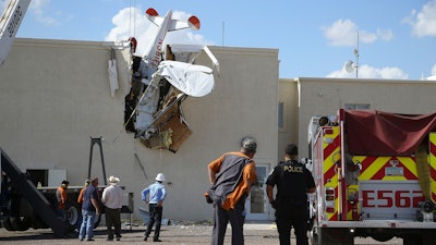 Police and fire personnel look on as workers remove a single-engine plane after it crashed into the terminal building at the Ak-Chin Regional Airport, Tuesday, Sept. 10, 2019, in Maricopa, Ariz.