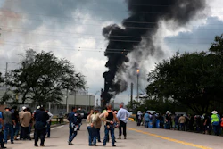 In this July 31, 2019, file photo, evacuated Exxon Mobil workers take a break or watch the fire from the Baytown Olefins Plant entrance in Baytown, Texas.