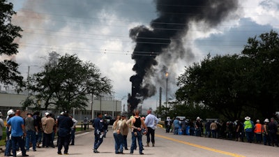 In this July 31, 2019, file photo, evacuated Exxon Mobil workers take a break or watch the fire from the Baytown Olefins Plant entrance in Baytown, Texas.