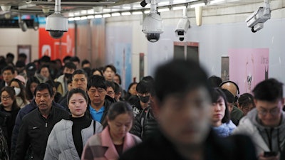 In this Feb. 26, 2019, file photo, commuters walk by surveillance cameras installed at a walkway in between two subway stations in Beijing.