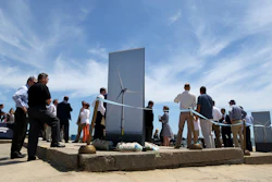 In this July 1, 2019, file photo, people gather around posters of wind turbines before Dominion Energy's groundbreaking ceremony for their offshore wind turbine project at Camp Pendleton in Virginia Beach, Va.