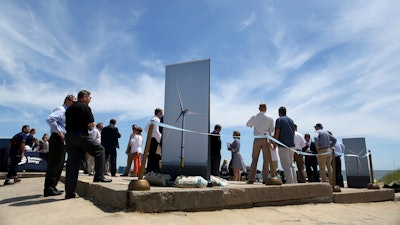 In this July 1, 2019, file photo, people gather around posters of wind turbines before Dominion Energy's groundbreaking ceremony for their offshore wind turbine project at Camp Pendleton in Virginia Beach, Va.