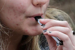 In this April 11, 2018, file photo, a high school student uses a vaping device near a school campus in Cambridge, Mass.