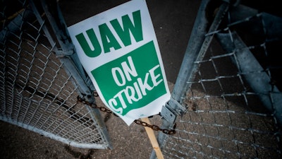 In this Monday, Sept. 16, 2019, file photo, a United Auto Workers strike sign rests between the chains of a locked gate entrance outside of Flint Engine Operations in Flint, Mich.