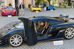 People looking at a 2015 Koenigsegg One:1 model car in front of a Aston Martin One-77 Coupe (2011), red, Ferrari LaFerrari (2015), yellow, and a Bugatti Veyron EB 16.4 Coupe (2010), blue, part of some 25 luxury cars owned by Teodoro Obiang, the son of the Equatorial Guinea's President Teodoro Obiang Nguema Mbasogo are pictured before an auction of sales house Bonhams at the Bonmont Abbey Golf & Country Club in Cheserex near Geneva, Switzerland, Sunday, Sept. 29, 2019. A collection of luxury cars from Equatorial Guinea's vice president Teodorin Obiang Nguema confiscated by the Geneva prosecutor's office after a deal ending a money-laundering inquiry, are auctioned off in Switzerland and are estimated to bring in 18.5 million Swiss francs.