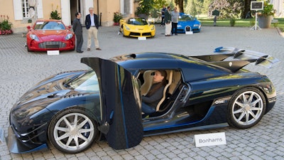 People looking at a 2015 Koenigsegg One:1 model car in front of a Aston Martin One-77 Coupe (2011), red, Ferrari LaFerrari (2015), yellow, and a Bugatti Veyron EB 16.4 Coupe (2010), blue, part of some 25 luxury cars owned by Teodoro Obiang, the son of the Equatorial Guinea's President Teodoro Obiang Nguema Mbasogo are pictured before an auction of sales house Bonhams at the Bonmont Abbey Golf & Country Club in Cheserex near Geneva, Switzerland, Sunday, Sept. 29, 2019. A collection of luxury cars from Equatorial Guinea's vice president Teodorin Obiang Nguema confiscated by the Geneva prosecutor's office after a deal ending a money-laundering inquiry, are auctioned off in Switzerland and are estimated to bring in 18.5 million Swiss francs.