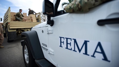 In this Oct. 5, 2017 file photo, Department of Homeland Security personnel deliver supplies to Santa Ana community residents in the aftermath of Hurricane Maria in Guayama, Puerto Rico. Federal authorities said Tuesday, Sept. 10, 2019, that they have arrested two former officials of the Federal Emergency Management Authority and the former president of a major disaster relief contractor, accusing them of bribery and fraud in the efforts to restore electricity to Puerto Rico in the wake of Hurricane Maria.