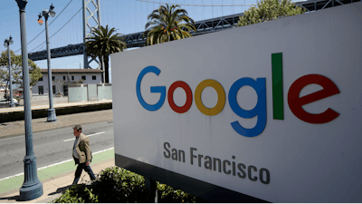 In this May 1, 2019, file photo a man walks past a Google sign outside with a span of the Bay Bridge at rear in San Francisco. A group of states are expected to announce an investigation into Google on Monday, Sept. 9, to investigate whether the tech company has become too big.