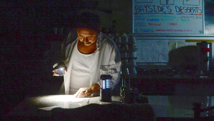 Carlos Lama of Bayside Cafe uses an LED lamp and light from his phone at the counter of the restaurant in Sausalito, Calif., Oct. 9, 2019.