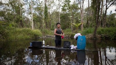 In this Sept. 2, 2019 photo, a young man washes his clothes in a pond in the viallge Ka 'a kyr, in Para state, Brazil.