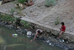 In this Sept. 26, 2019, photo, a girl from an impoverished family reaches out to grab a plastic bottle from a canal in New Delhi.