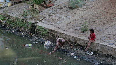 In this Sept. 26, 2019, photo, a girl from an impoverished family reaches out to grab a plastic bottle from a canal in New Delhi.