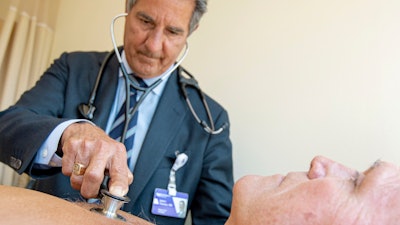 In this July 8, 2019 photo, James Thomas, a cardiologist at Northwestern Hospital in Chicago, examines Dennis Calling, a retired Chicago inspector.