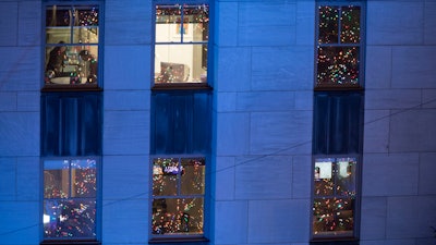 In this Nov. 28, 2018, file photo people work in their office after the Rockefeller Center Christmas tree is lit during the 86th annual Rockefeller Center Christmas tree lighting ceremony in New York. Holiday staffing is one of a small business owner’s biggest stressors. Even companies that aren’t retailers or restaurants can have a year-end busy season, just when employees all want to take time off.