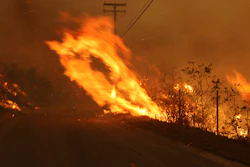 In this Nov. 9, 2018 file photo Wind-driven flames from a wildfire race up a slope and cross the road in Malibu, Calif. known as the Woolsey Fire, it has consumed tens of thousands of acres and destroyed multiple homes. Southern California Edison announced in its quarterly earnings report that its equipment probably caused the November 2018 Woolsey Fire that raged from north of Los Angeles through Malibu to the sea, killing three people and burning more than 1,600 homes and other buildings.