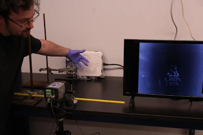 Paper lead author and University of Arizona graduate student Tristan Klein demonstrates the lens's transparency to infrared light.