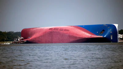 In this Sept. 9, 2019, file photo, a Moran tugboat nears the stern of the capsizing vessel Golden Ray as a tent and rescuers can be seen near the bottom of the ship near the tug boat in Jekyll Island, Ga. Marine salvage experts seeking to remove the overturned cargo ship close to Georgia's seacoast will haul it away in pieces because it cannot be safely righted and refloated intact, their Unified Command said in a statement Saturday, Oct. 12.