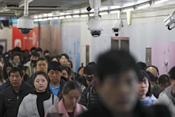 In this Feb. 26, 2019, file photo, commuters walk by surveillance cameras installed at a walkway in between two subway stations in Beijing.