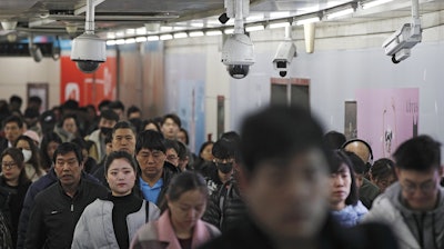 In this Feb. 26, 2019, file photo, commuters walk by surveillance cameras installed at a walkway in between two subway stations in Beijing.