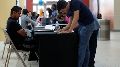 In this Oct. 1, 2019, file photo, Billy Ramos, right, fills out a job application with Adidas during a job fair at Dolphin Mall in Miami.