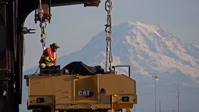In this Nov. 4, 2019, photo, a worker prepares Caterpillar construction equipment to be lifted off a trailer at the Port of Tacoma, Wash.